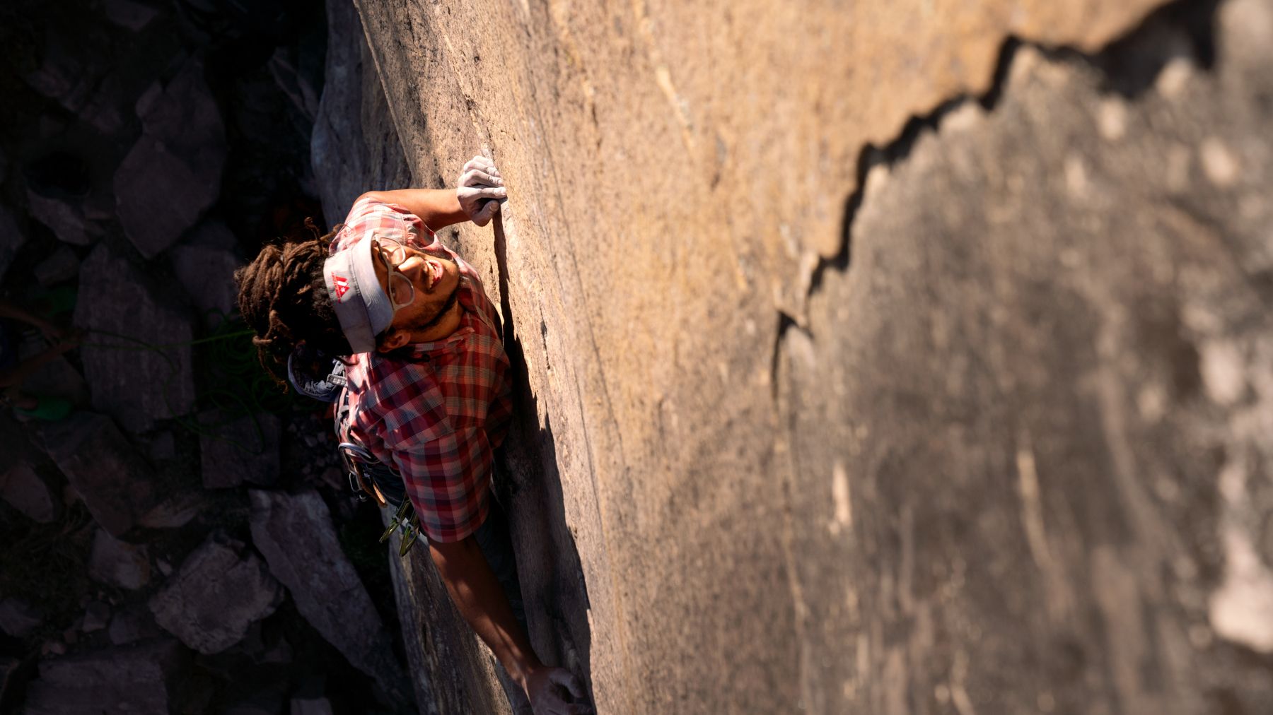A climber works a crack up a sunlit rock face.